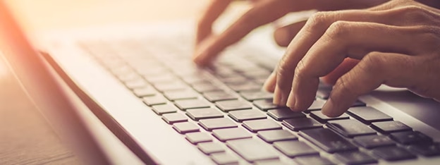 Close-up of hands typing on a laptop keyboard, representing routine maintenance for a clean PC